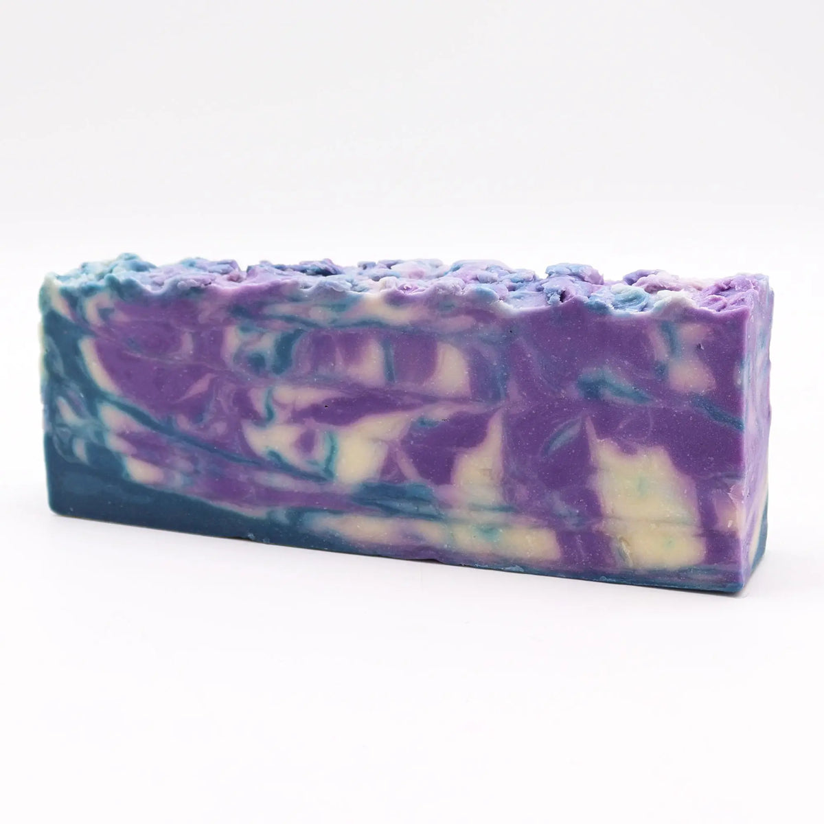 Barra de jabón artesanal con remolinos de colores morado, azul y blanco sobre un fondo blanco limpio y minimalista