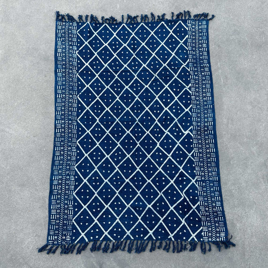 Alfombra azul marino con diseño geométrico blanco y flecos, hecha de algodón. Ideal para decoración moderna.