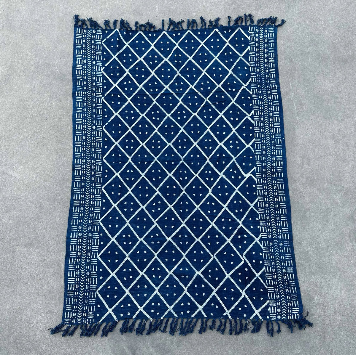 Alfombra azul marino con diseño geométrico blanco y flecos, hecha de algodón. Ideal para decoración moderna.