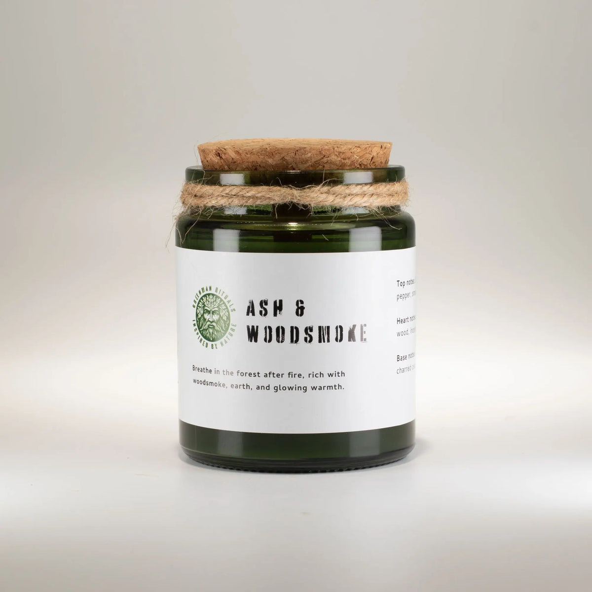 Vela de vidrio verde "Ash & Woodsmoke" con tapa de madera, aroma a tierra y humo de leña, estilo rústico.