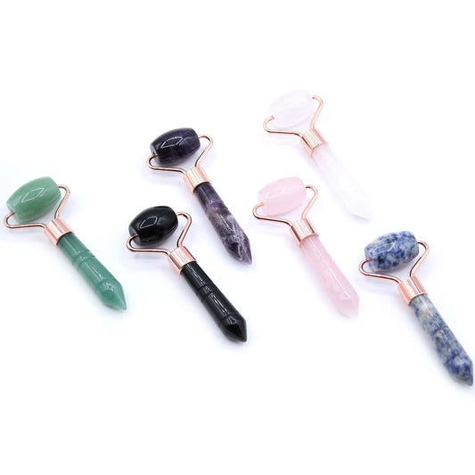 Seis mini rodillos faciales de piedras preciosas de colores con mangos en punta y herrajes metálicos en tono oro rosa.