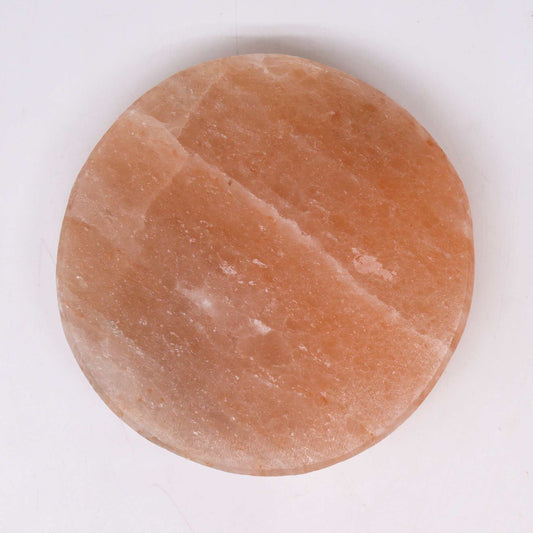 Plato redondo de sal del Himalaya con textura cristalina en tonos rosados, sobre un fondo blanco neutro.