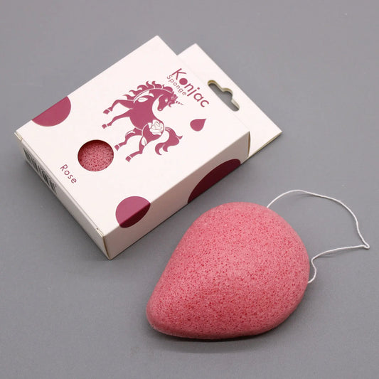 Esponja facial de konjac rosa en forma de gota con cordón junto a su caja de cartón con dibujo de unicornio.