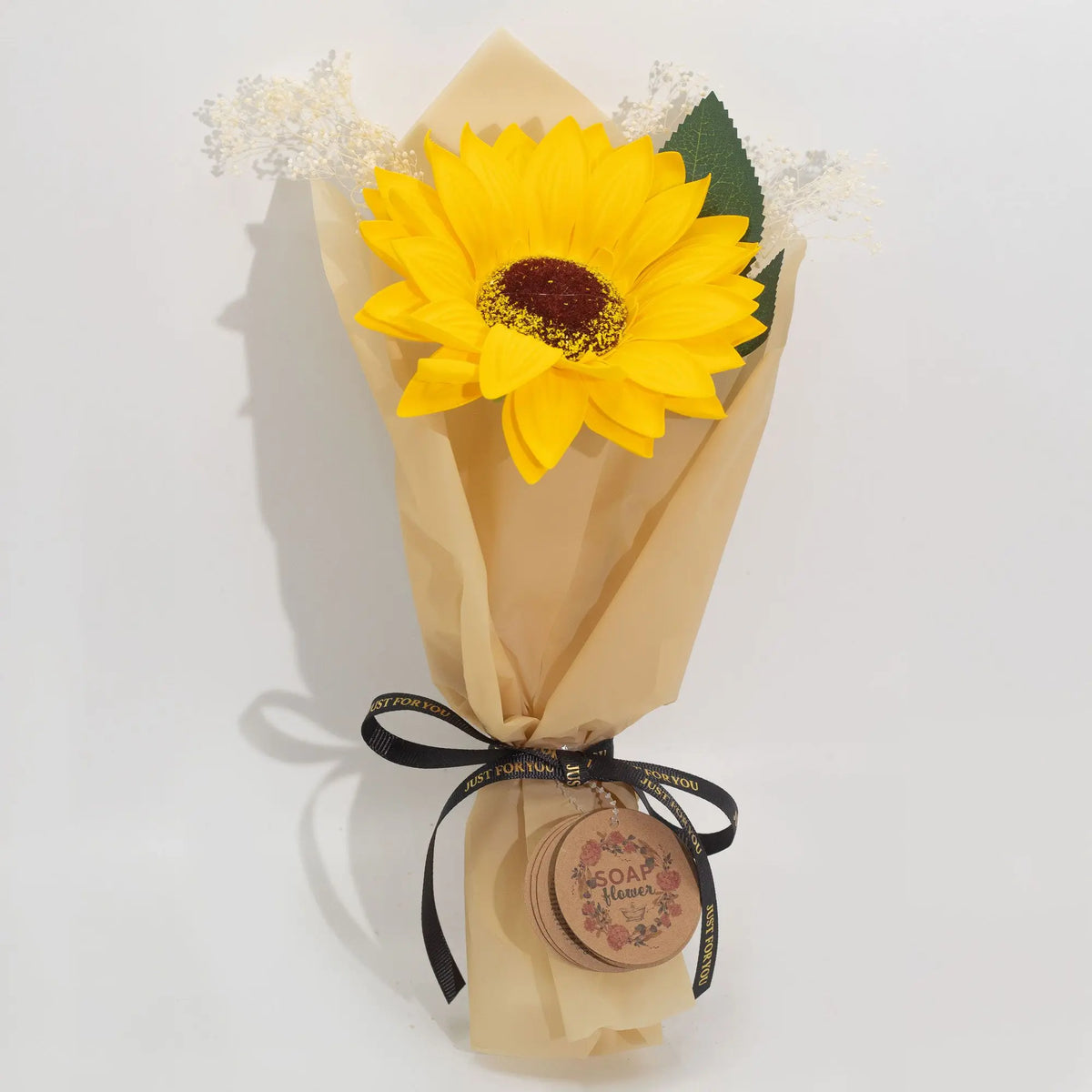 Girasol de jabón amarillo envuelto en papel beige, decorado con cinta negra y flores blancas secas.