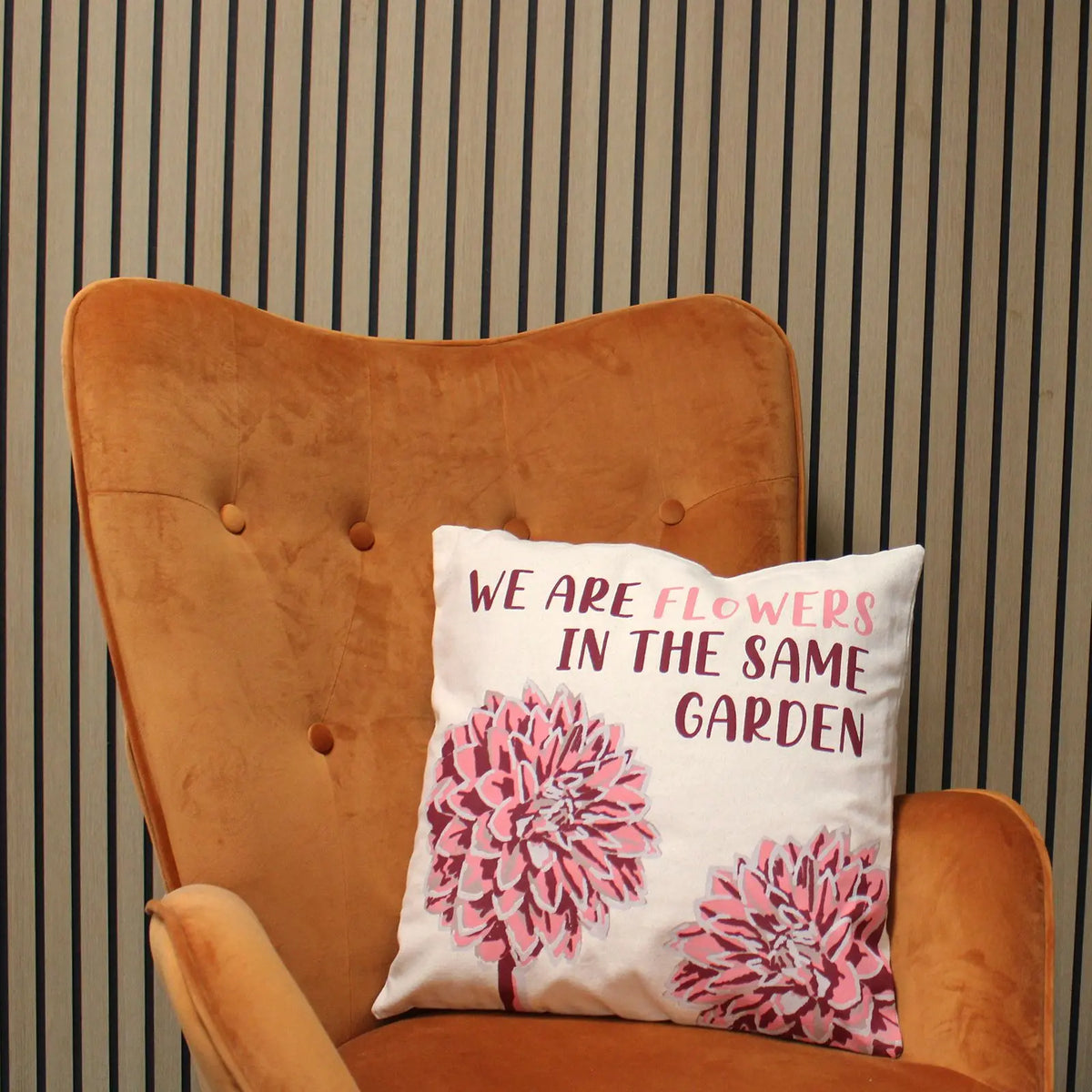 Funda de cojín de algodón con estampado floral rosa y texto sobre sillón tapizado color ámbar.