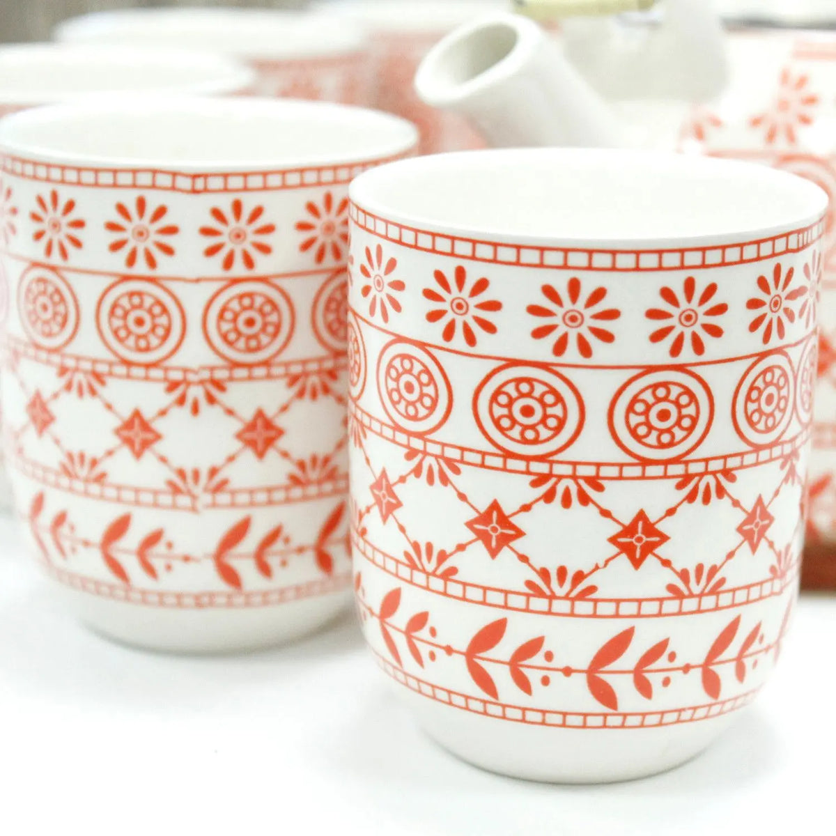 Set de cerámica con tetera y tazas blancas estampadas con motivos geométricos y florales en color ámbar rojizo