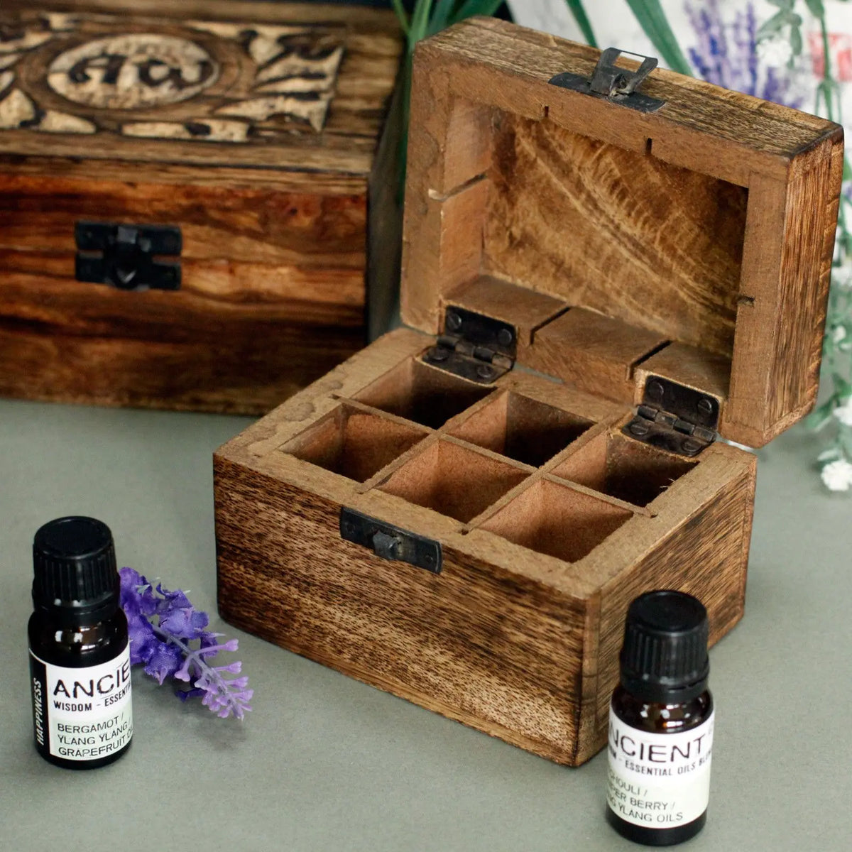 Caja de madera de mango rústica con 6 compartimentos, bisagras metálicas y cierres, junto a frascos de aceites esenciales.