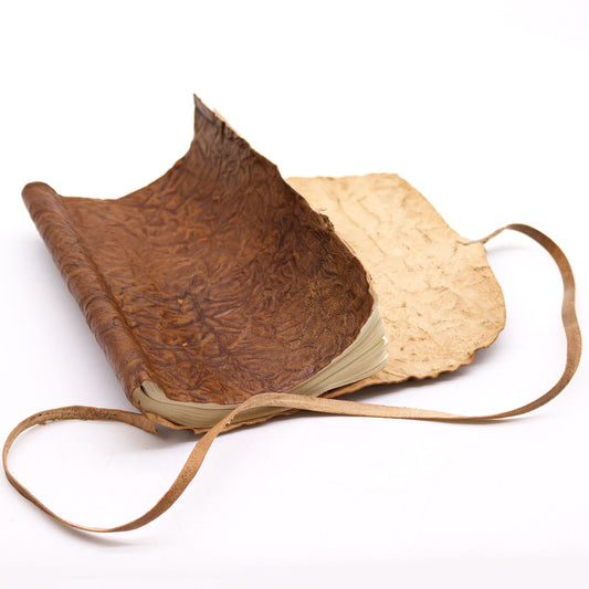 Cuaderno de cuero marrón con papel crudo, diseño rústico y tapa de textura arrugada. Ideal para notas y bocetos.