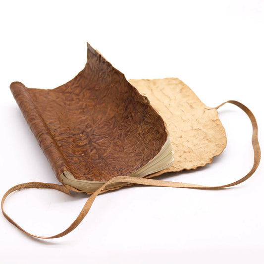 Cuaderno de cuero marrón con papel crudo, diseño rústico y tapa de textura arrugada. Ideal para notas y bocetos.
