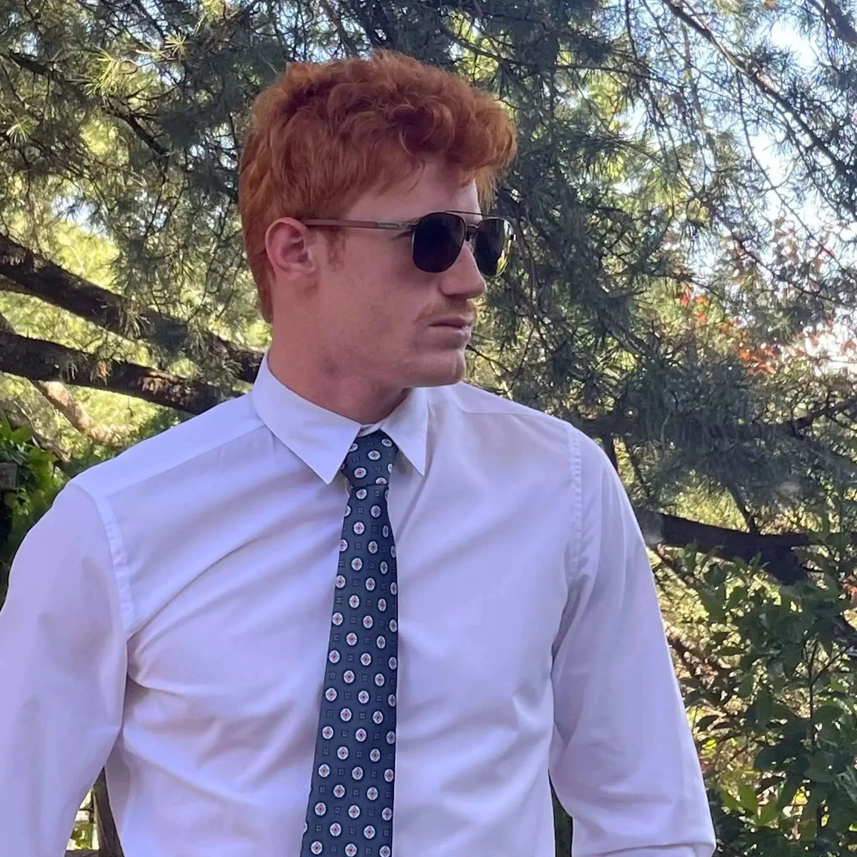 Gafas de sol estilo aviador con montura de madera oscura y cristales oscuros sobre un hombre de cabello pelirrojo.