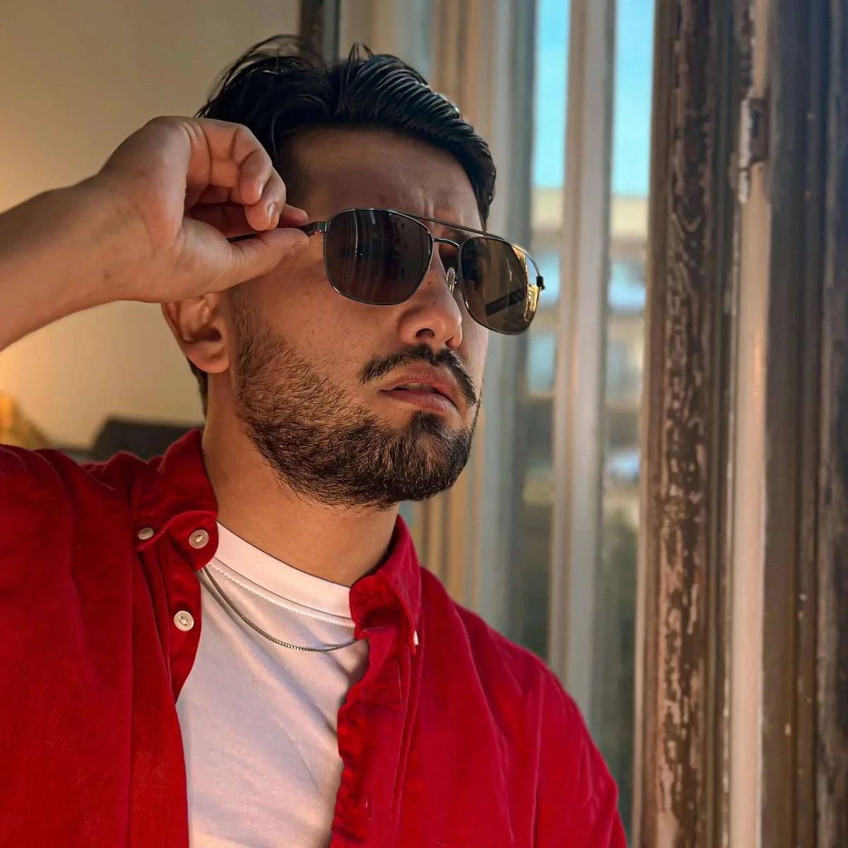 Hombre con gafas de sol estilo aviador, montura de madera oscura y lentes ahumadas, luciendo una camisa roja.