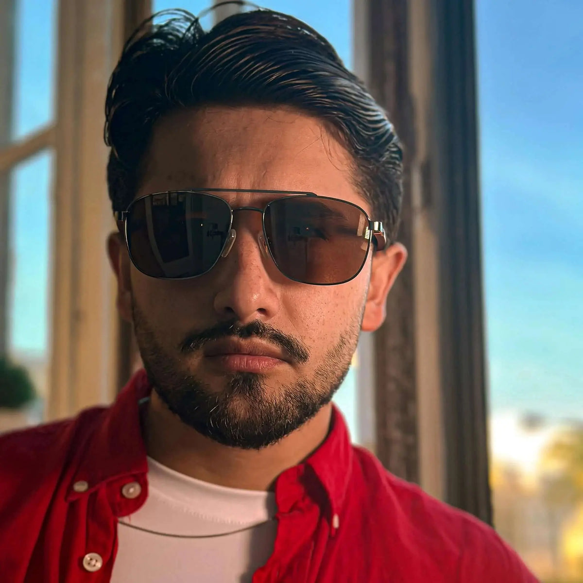 Gafas de sol tipo aviador con marco de madera oscura y lentes ahumados oscuros sobre un hombre joven.