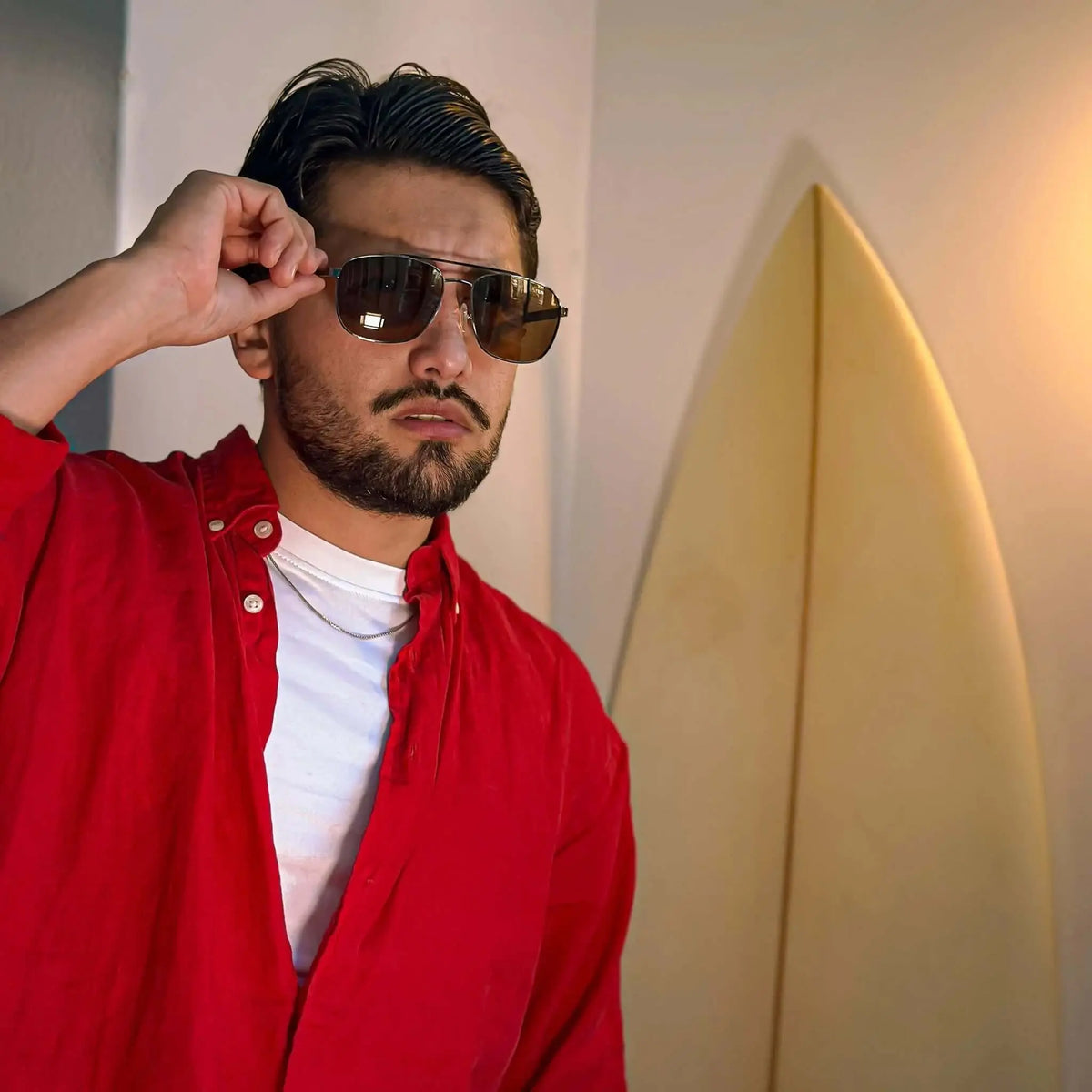 Hombre con gafas de sol tipo aviador, montura de madera y metal, cristales oscuros y camisa roja.