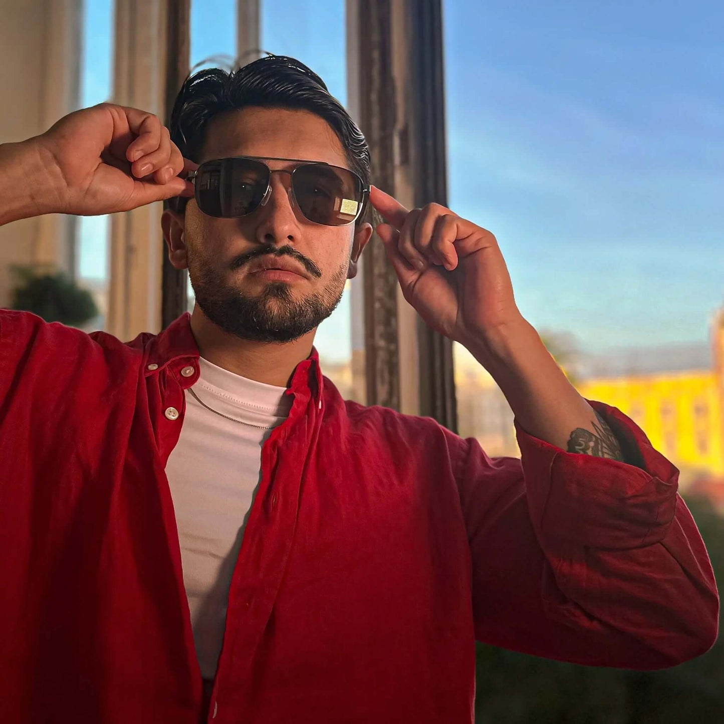 Gafas de sol tipo aviador con marco de madera oscura y cristales oscuros, usadas por un hombre con camisa roja.