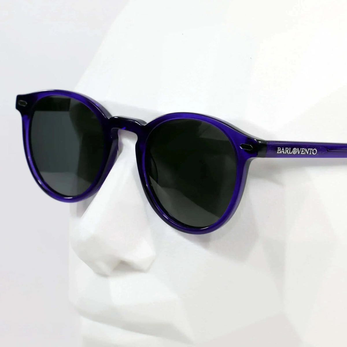 Gafas de sol de montura redonda en plástico traslúcido color morado con lentes oscuras sobre maniquí blanco.