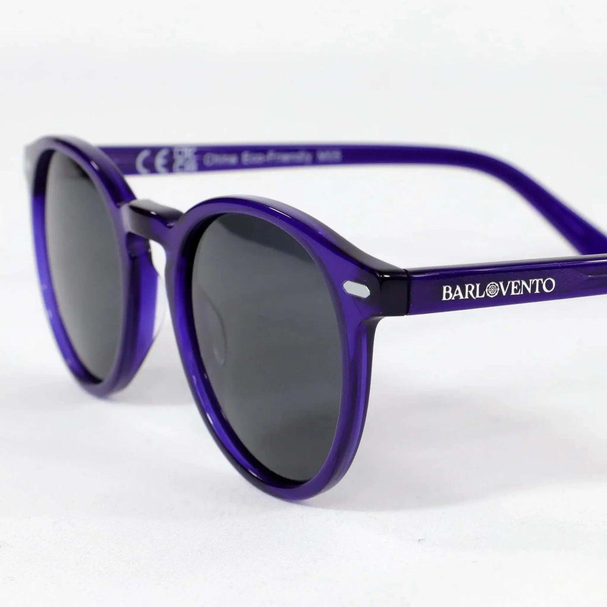 Gafas de sol redondas con montura de acetato translúcido color morado y cristales oscuros sobre fondo blanco.