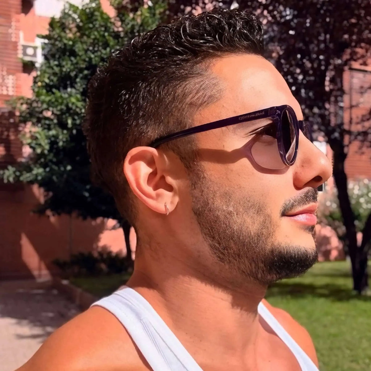 Gafas de sol de montura redonda en color púrpura oscuro con lentes degradadas, lucidas por un hombre de perfil.