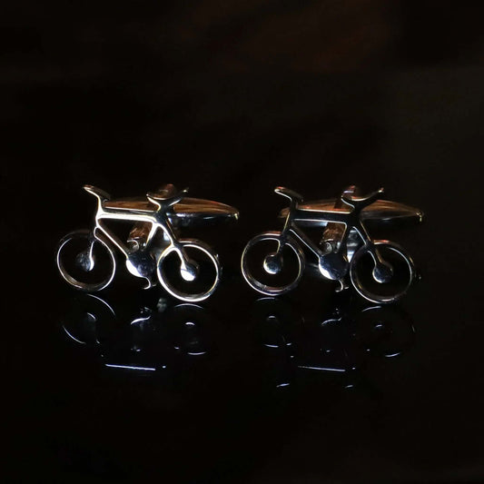 Gemelos de metal plateado con forma de bicicleta sobre fondo oscuro, con acabado brillante y diseño detallado.