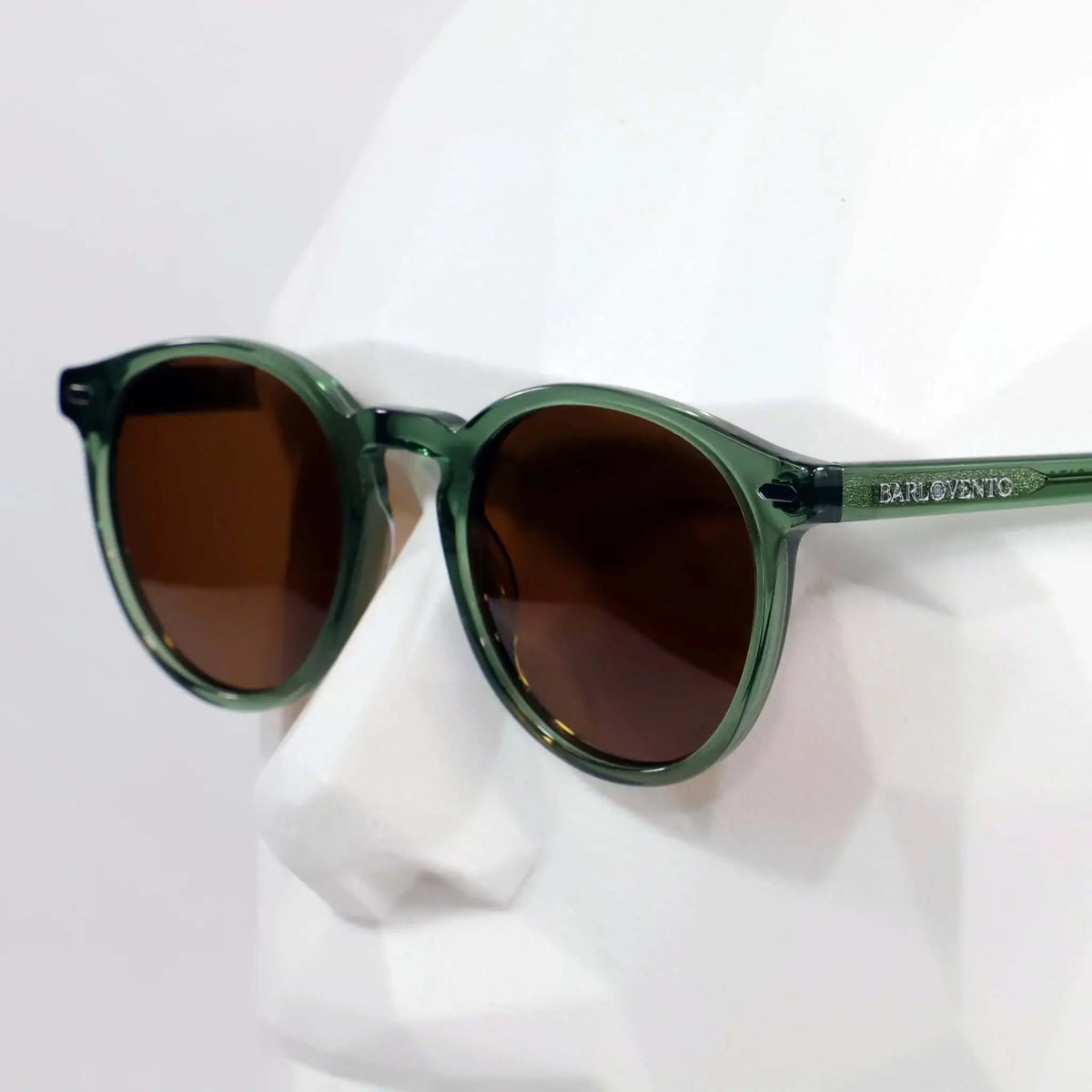 Gafas de sol redondas con montura de acetato translúcido verde y lentes oscuras de tono marrón.