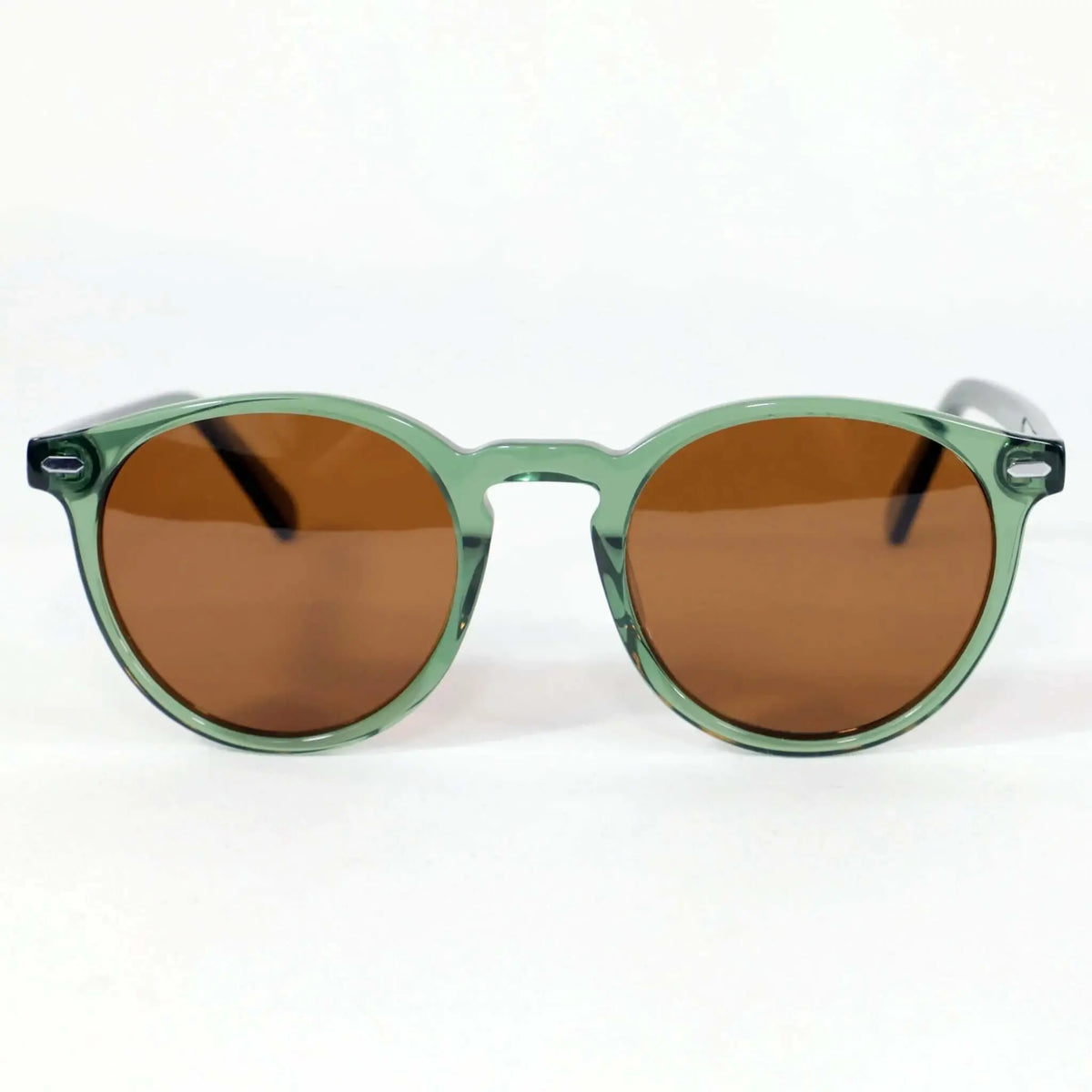 Gafas de sol redondas con montura de acetato verde translúcido y lentes marrones sobre fondo blanco.