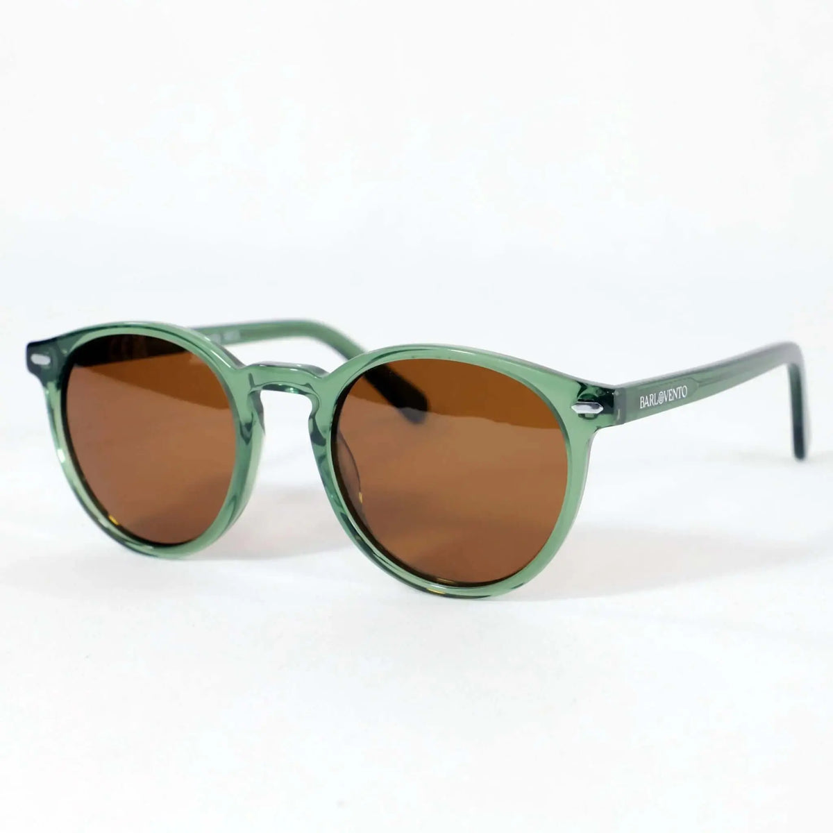 Gafas de sol de montura redonda en acetato verde translúcido con lentes color café sobre fondo blanco.