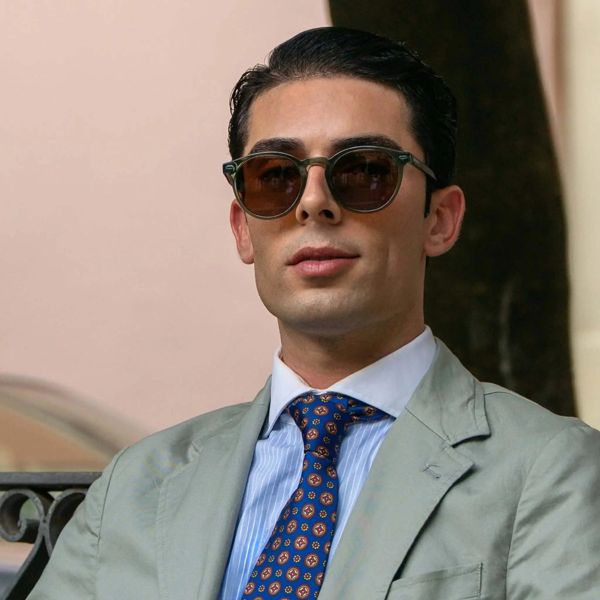 Hombre elegante con gafas de sol redondas de montura verde translúcida y lentes marrones oscuras.