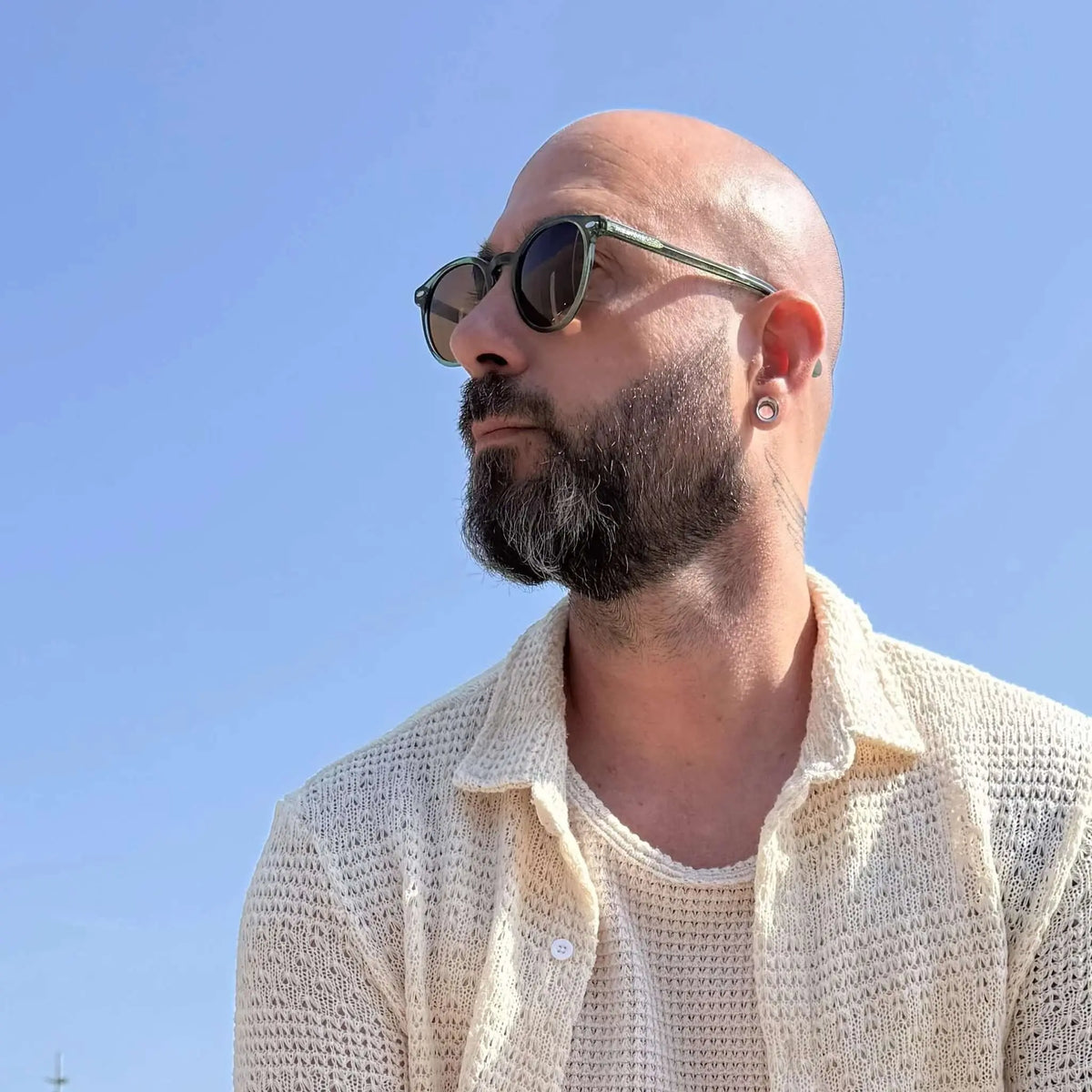 Gafas de sol redondas con montura de acetato verde translúcido y lentes marrones sobre un hombre con barba.