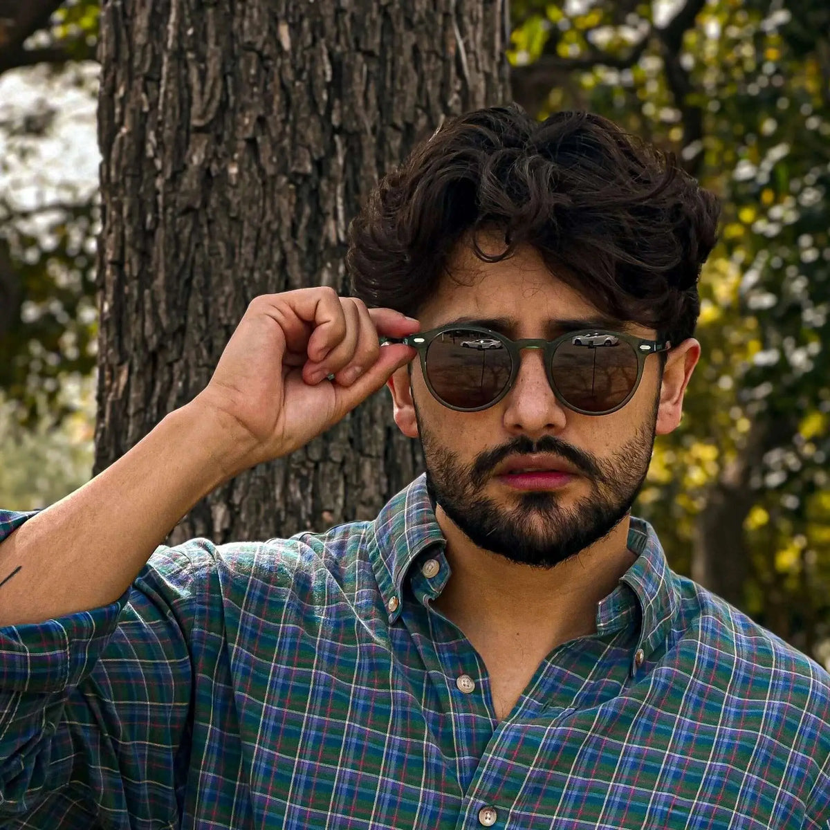 Gafas de sol redondas con montura verde mate y cristales oscuros, lucidas por un hombre con camisa a cuadros.