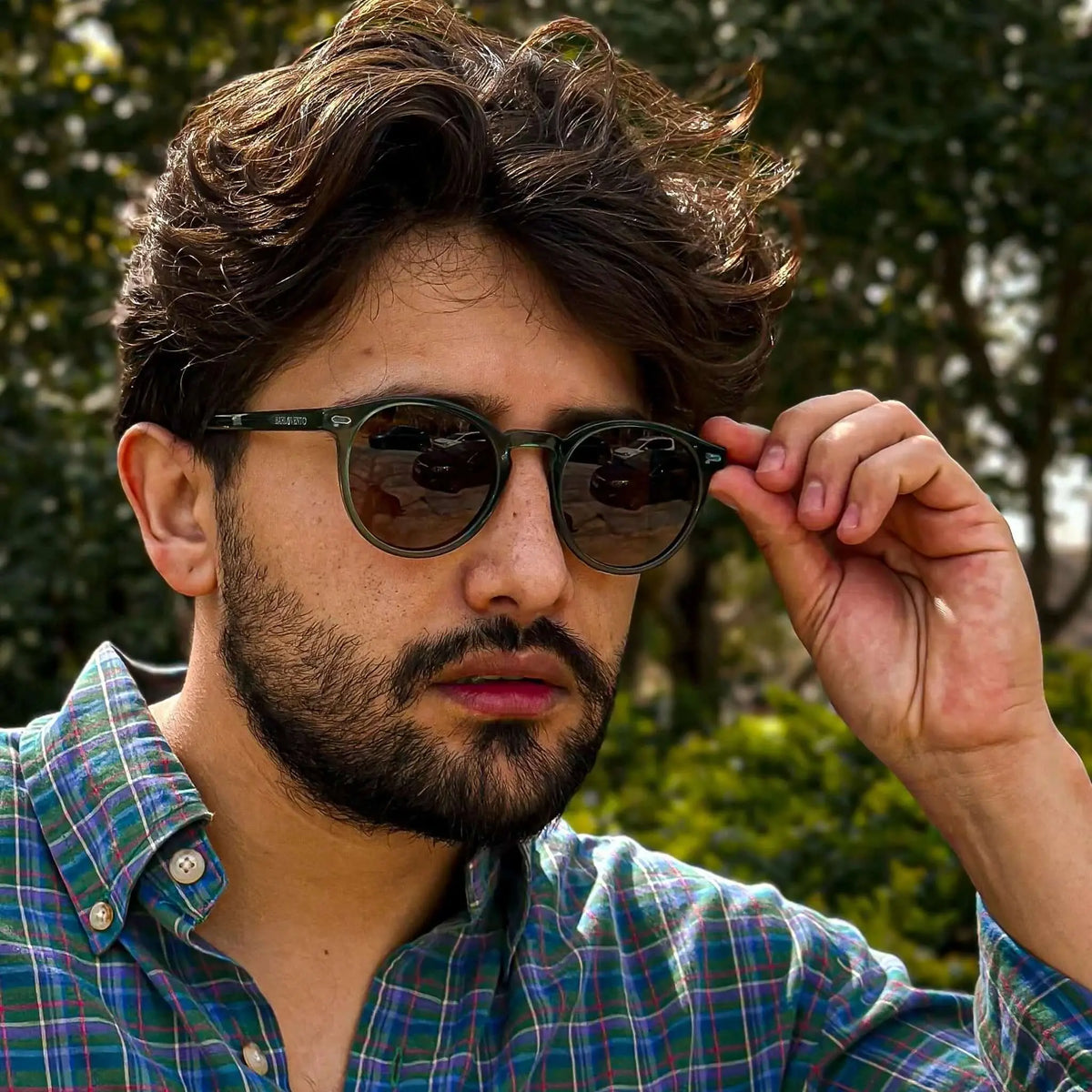 Hombre con gafas de sol redondas de montura verde translúcida y cristales oscuros, estilo casual.
