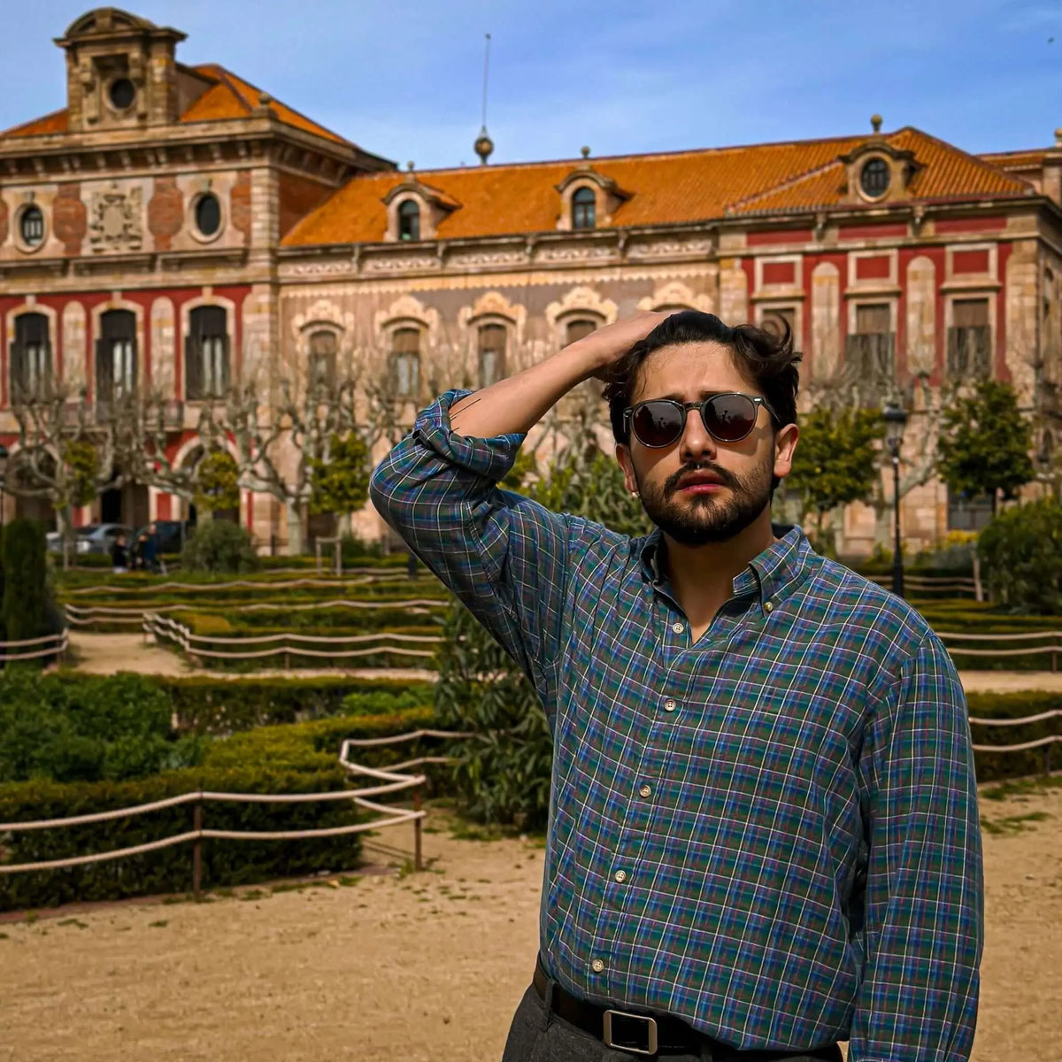 Gafas de sol redondas con montura verde y lentes marrones. Estilo clásico ante un edificio histórico.