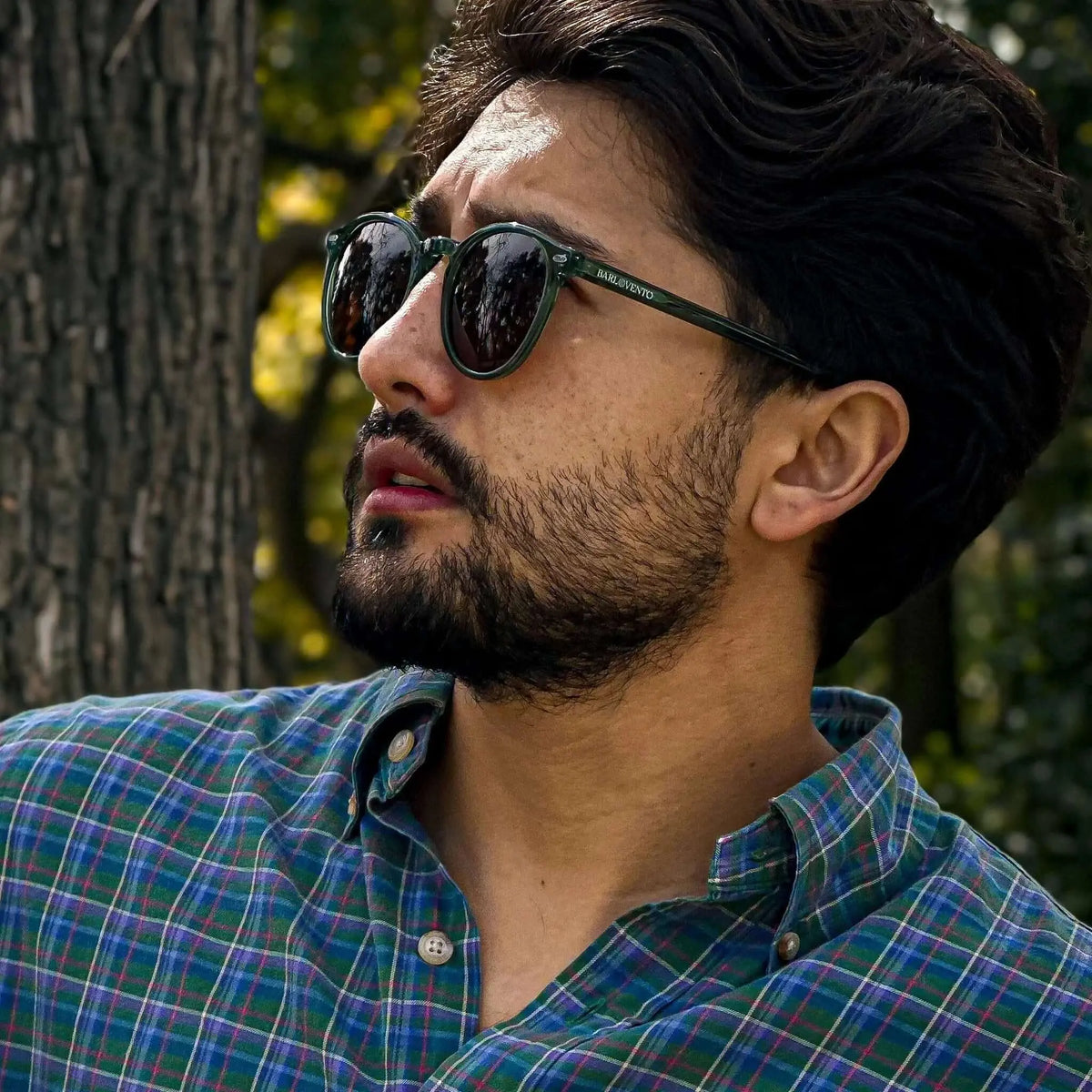 Gafas de sol redondas con montura verde translúcida y lentes oscuras de estilo clásico puestas en un hombre.
