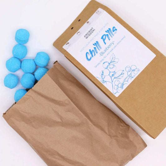 Mini bombas de baño azules con forma cilíndrica saliendo de una bolsa de papel kraft junto a una caja de cartón.