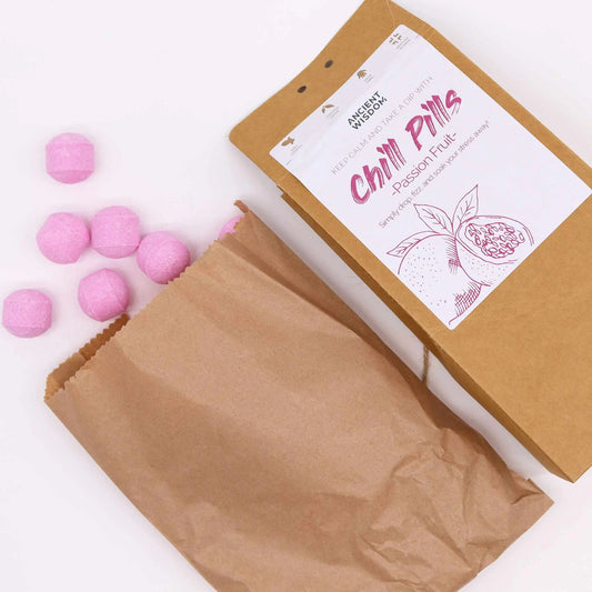 Mini bombas de baño rosas junto a una bolsa de papel kraft con etiqueta de fruta de la pasión sobre fondo blanco.