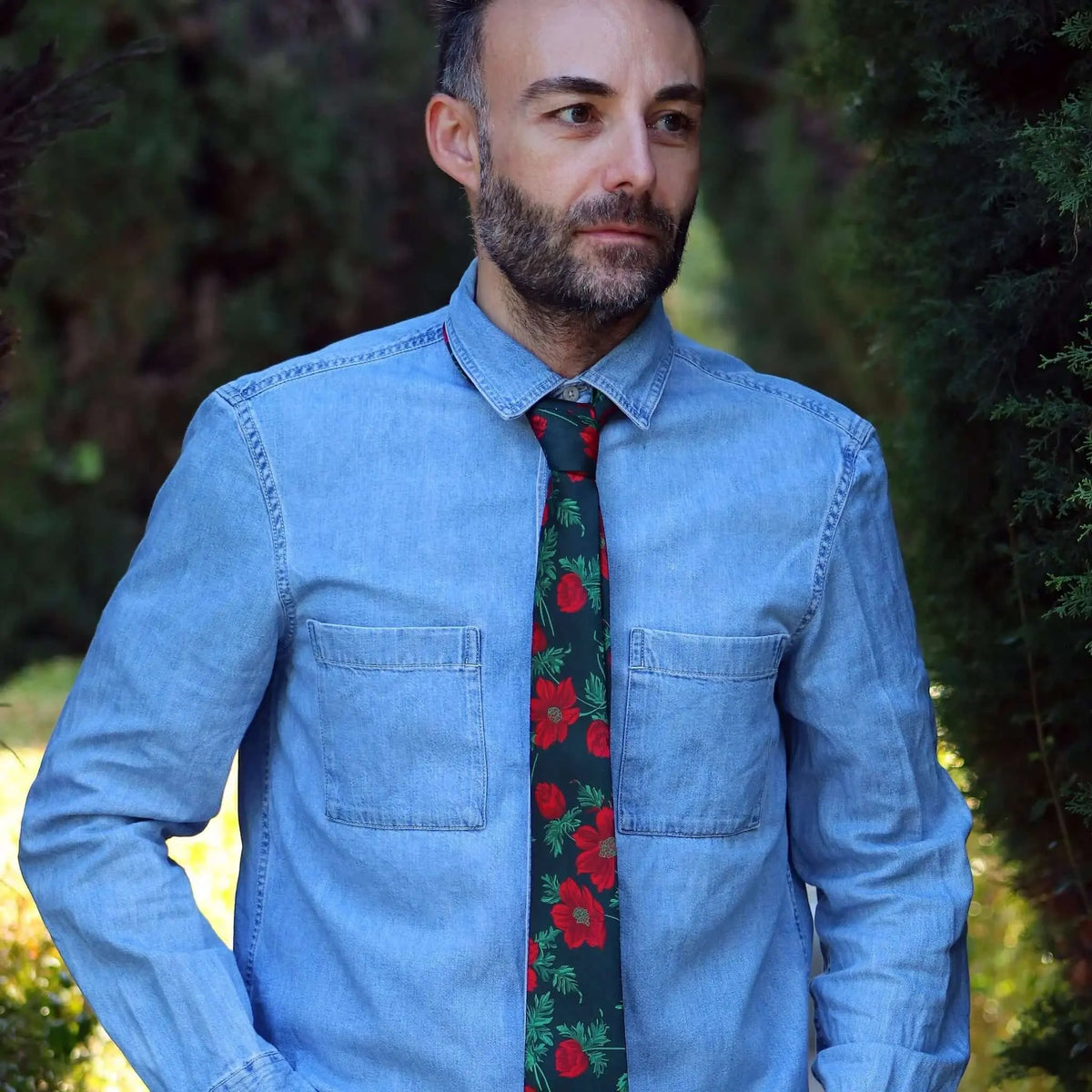 Corbata verde oscuro con estampado de flores rojas y hojas, sobre camisa de mezclilla azul. Estilo casual y elegante.