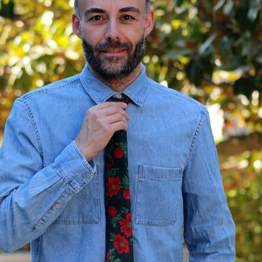 Corbata verde oscuro con estampado de flores rojas y hojas verdes sobre camisa de mezclilla azul.