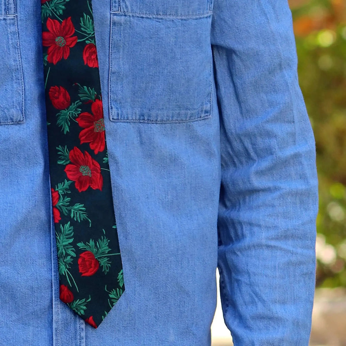 Corbata negra con estampado de flores rojas y hojas verdes sobre camisa de mezclilla azul.