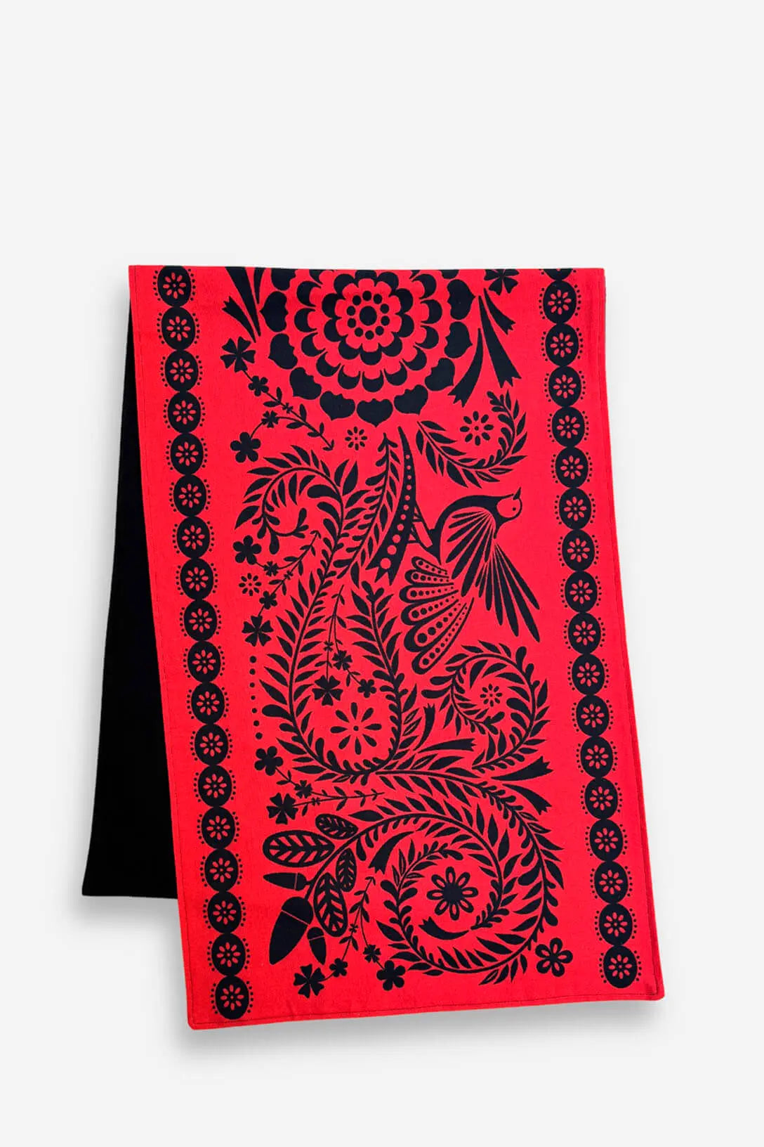 Camino de mesa rojo con estampado folclórico negro de aves y flores estilo artesanal sobre fondo blanco.