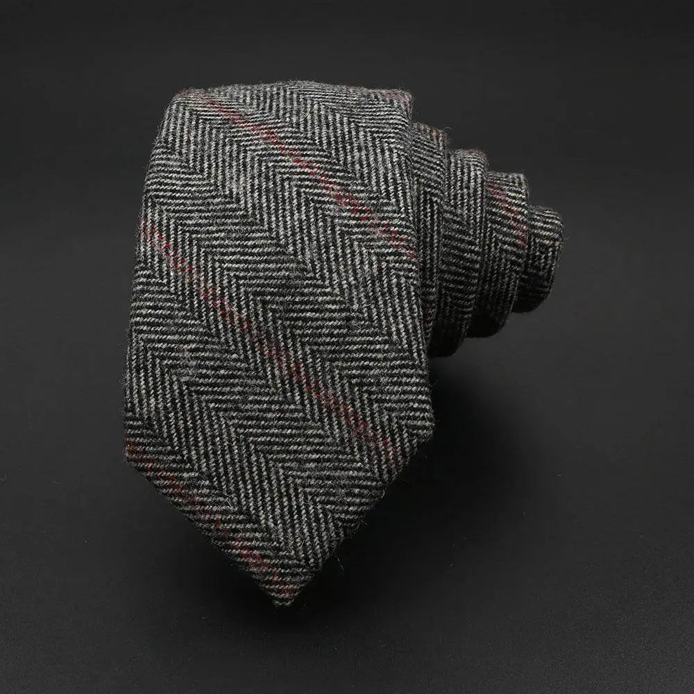 Corbata estrecha de lana gris con patrón de espiga y sutiles detalles en color rojo sobre fondo oscuro.