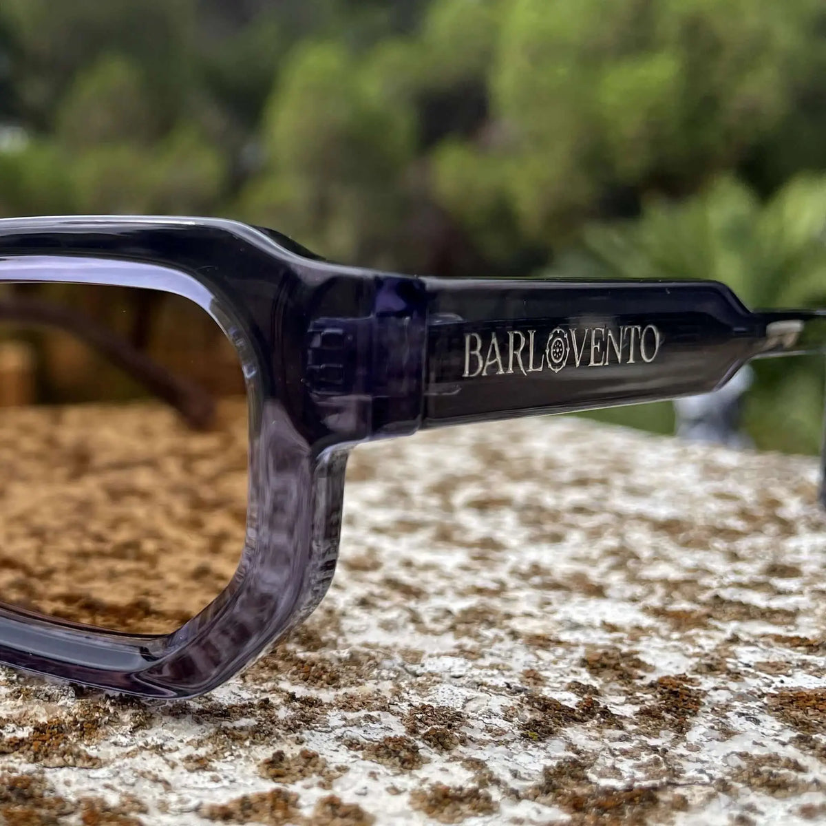 Gafas de sol con montura de acetato azul translúcido y lentes marrones sobre una superficie de piedra rústica.