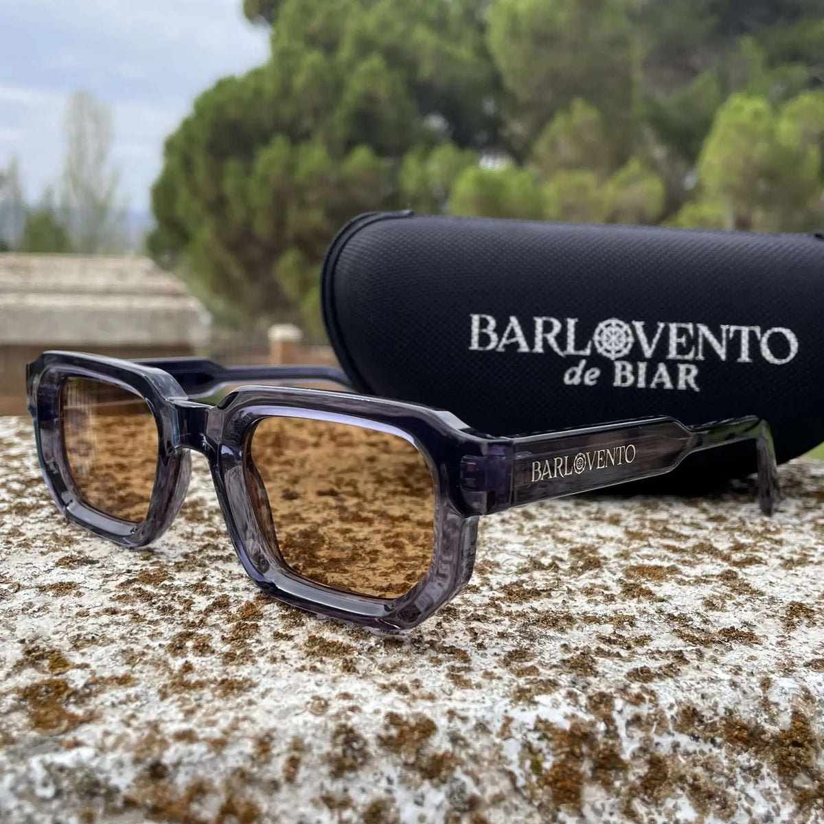 Gafas de sol rectangulares con montura de acetato azul translúcido y lentes marrones sobre una superficie de piedra.