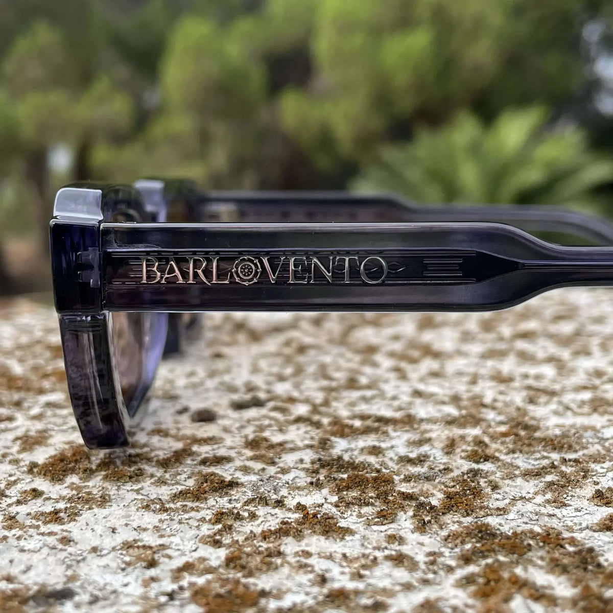 Gafas de sol de pasta azul traslúcida con diseño robusto y lentes en tono marrón, presentadas al aire libre.