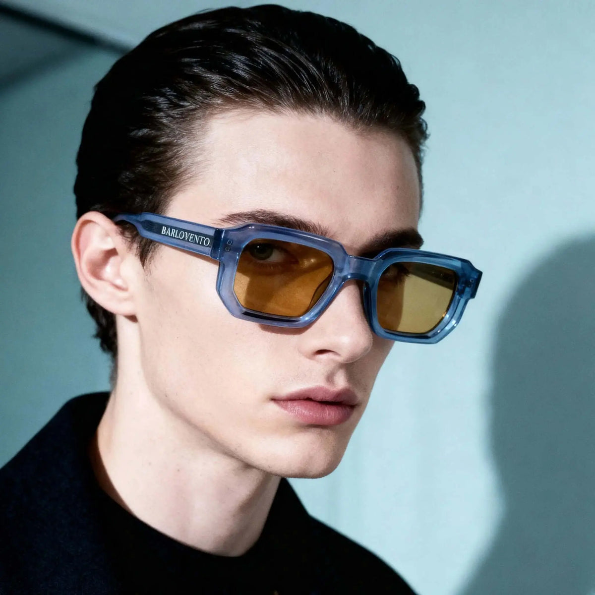 Gafas de sol rectangulares con montura azul traslúcida y lentes en tono ámbar puestas en un joven.