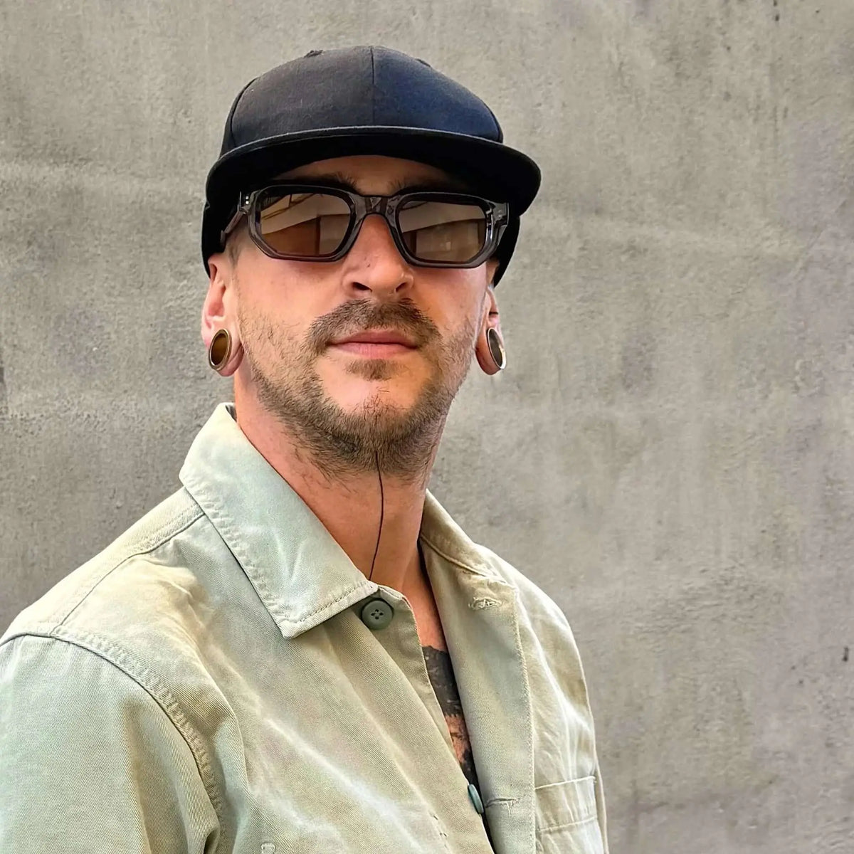 Gafas de sol de montura azul cuadrada y lentes marrones puestas por un hombre con gorra negra.