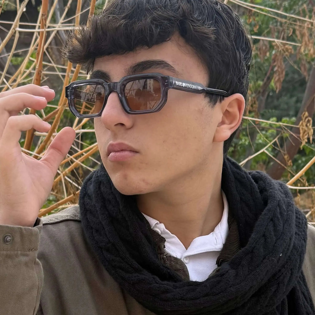 Gafas de sol rectangulares con montura azul traslúcida y lentes marrones puestas por un joven con bufanda negra.