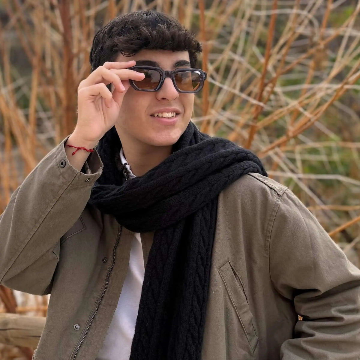 Gafas de sol de montura azul oscuro y forma rectangular con cristales marrones puestas por un joven con bufanda negra.
