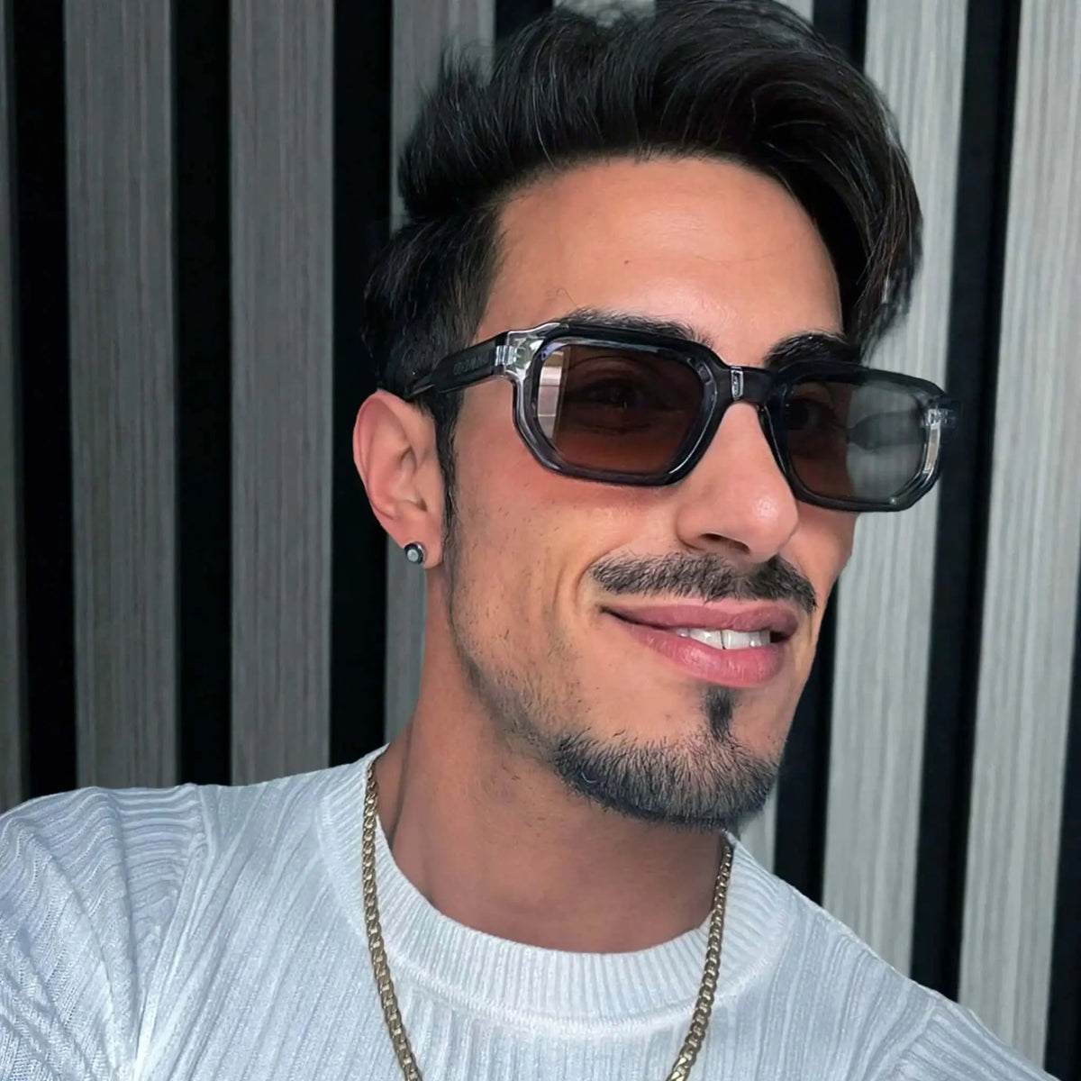 Hombre con gafas de sol de montura rectangular transparente en tono azulado y lentes marrones de estilo moderno.