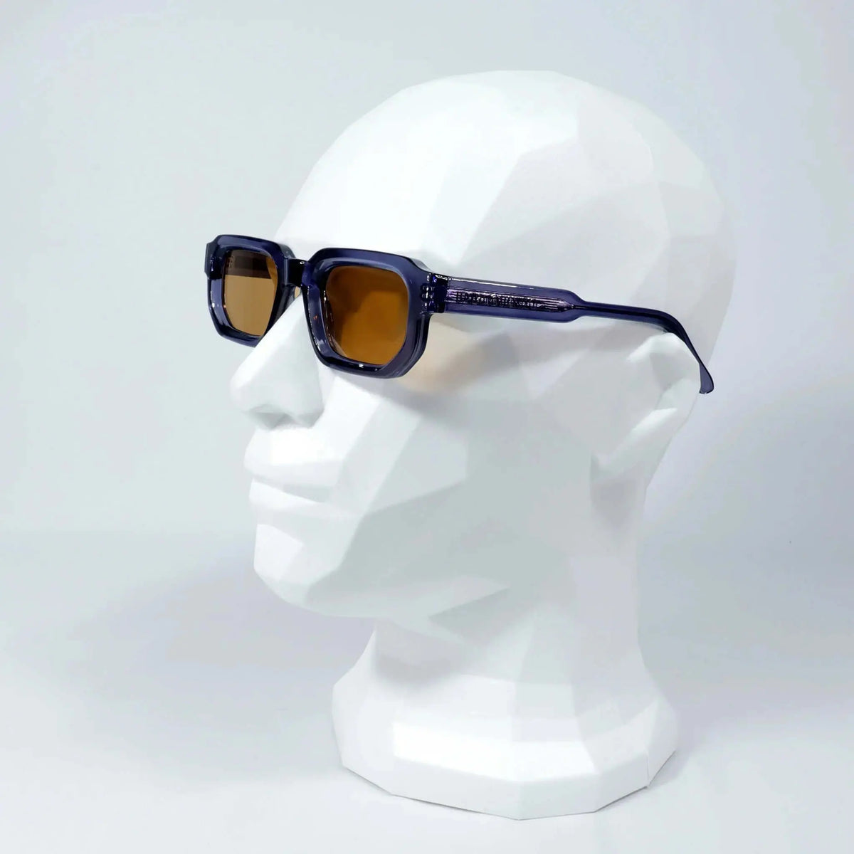 Gafas de sol de montura azul traslúcida y diseño rectangular con cristales en tono marrón, puestas sobre maniquí.