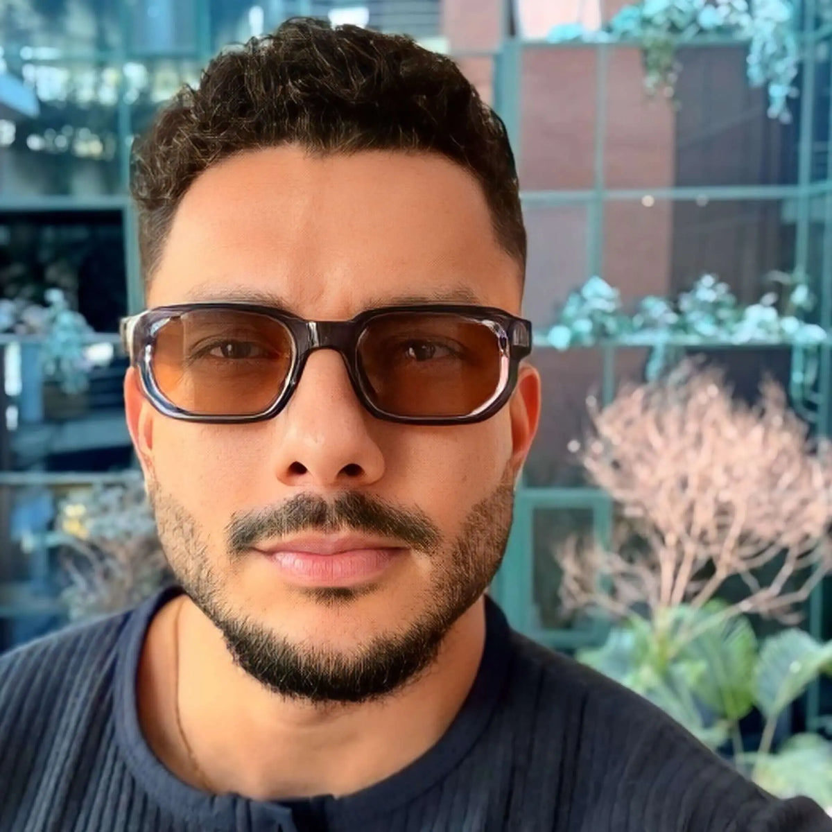 Hombre usando gafas de sol rectangulares con montura azul oscuro y lentes color marrón. Estilo moderno y elegante.