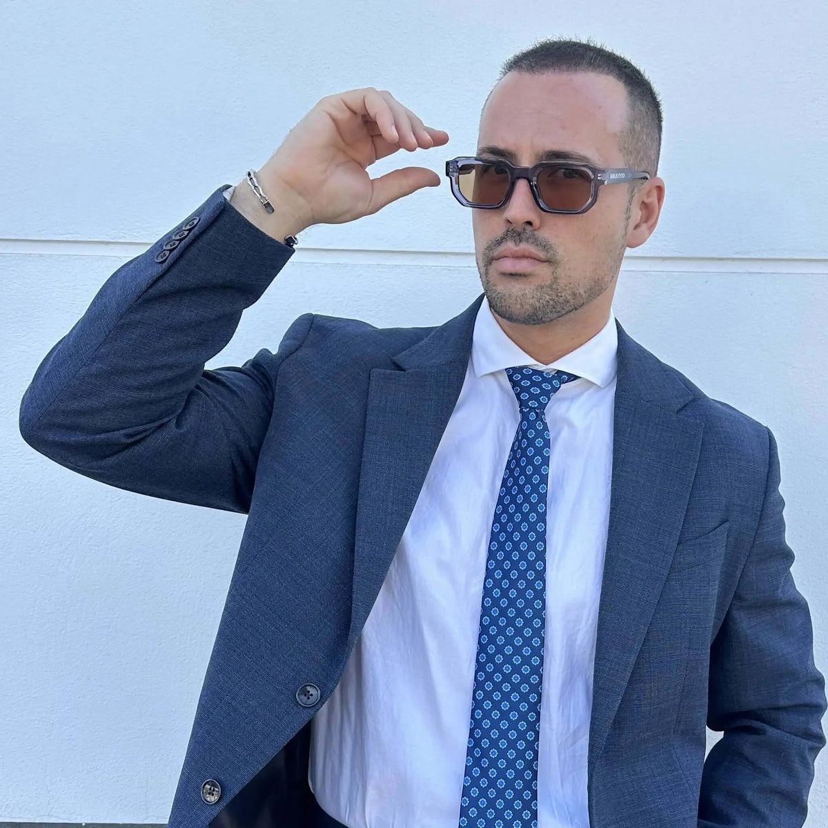 Gafas de sol de montura cuadrada azul translúcida y lentes marrones, estilo moderno, sobre un hombre con traje.
