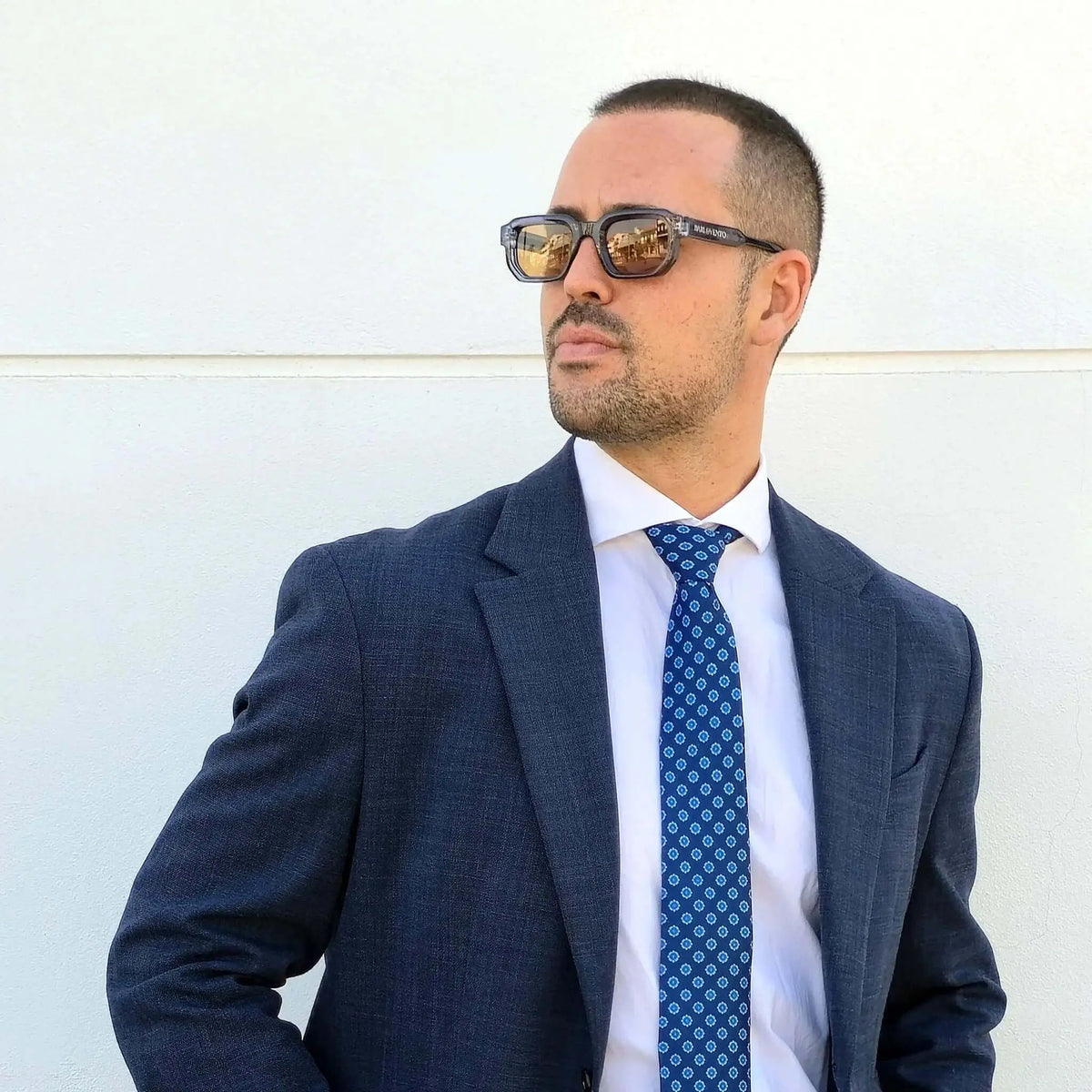 Hombre con traje y corbata usando gafas de sol de montura azul translúcida cuadrada y lentes marrones reflectantes.